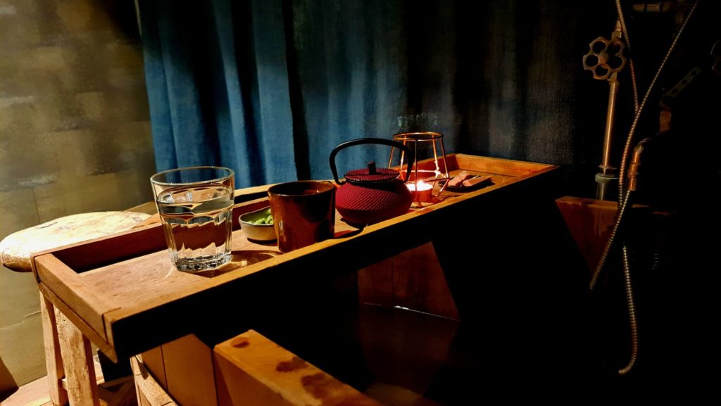 Pohár vody, čaj a wasabi oriešky na drevenej vani