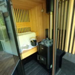 Otvorené dvere do kontajnerovej sauny. Plachta na lavici, sauna pec a vedro.